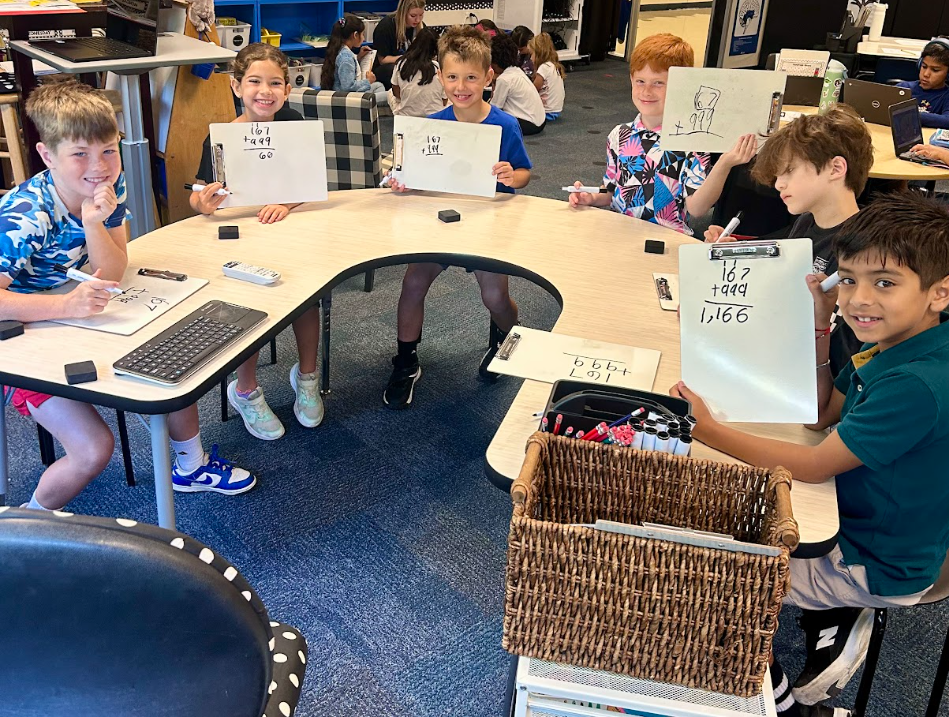 students sitting at a table together holding up white boards with math equations written on them