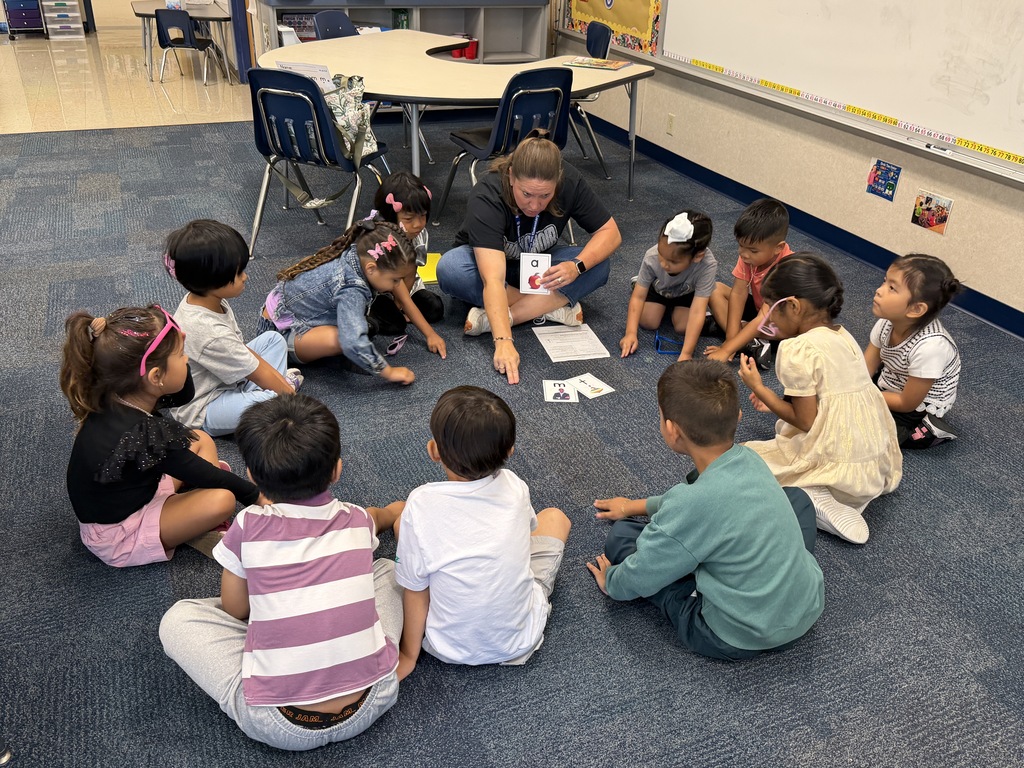 teacher working with a group of students on the floor with lettered flashcards