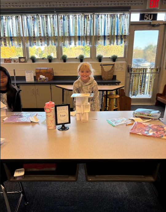 student smiling behind a tower made of index cards holding up a book