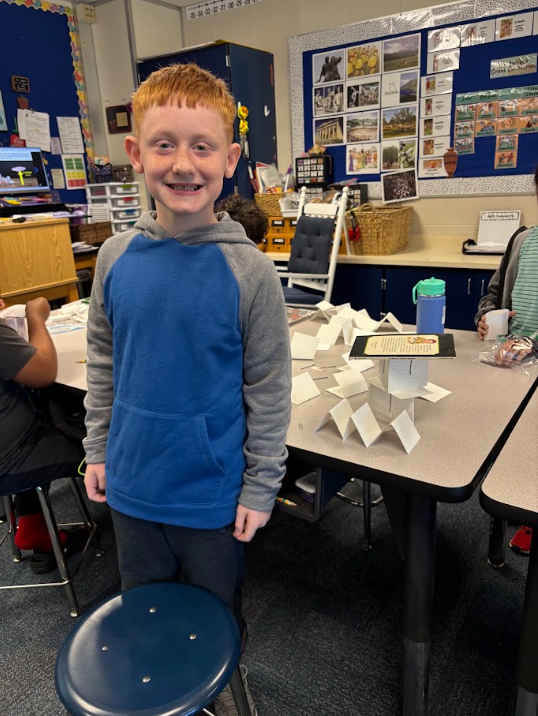 student smiling in front of a tower made of index cards holding up a book