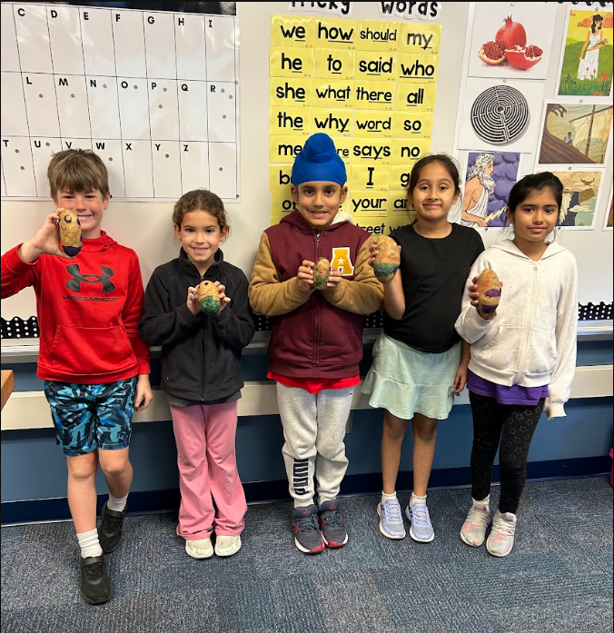 5 students smiling in a row as they hold up their decorated potatoes
