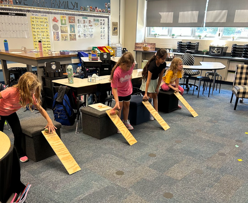 students rolling their potatoes down wooden boards
