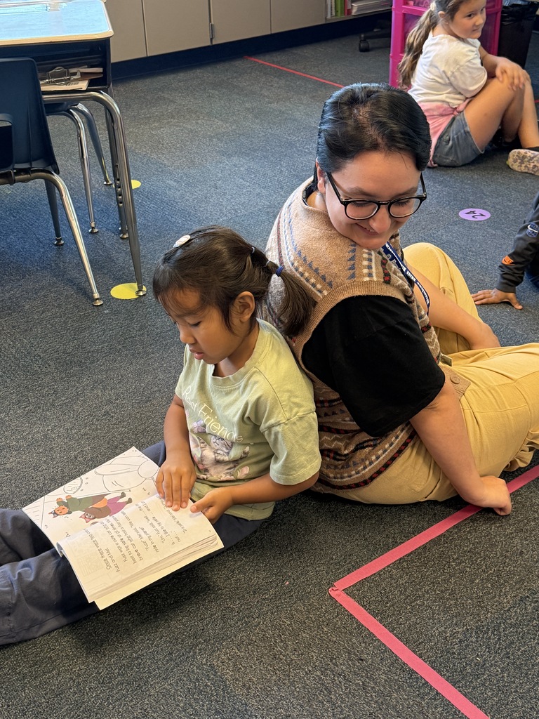student and teacher sitting back to back on the floor while student reads a book