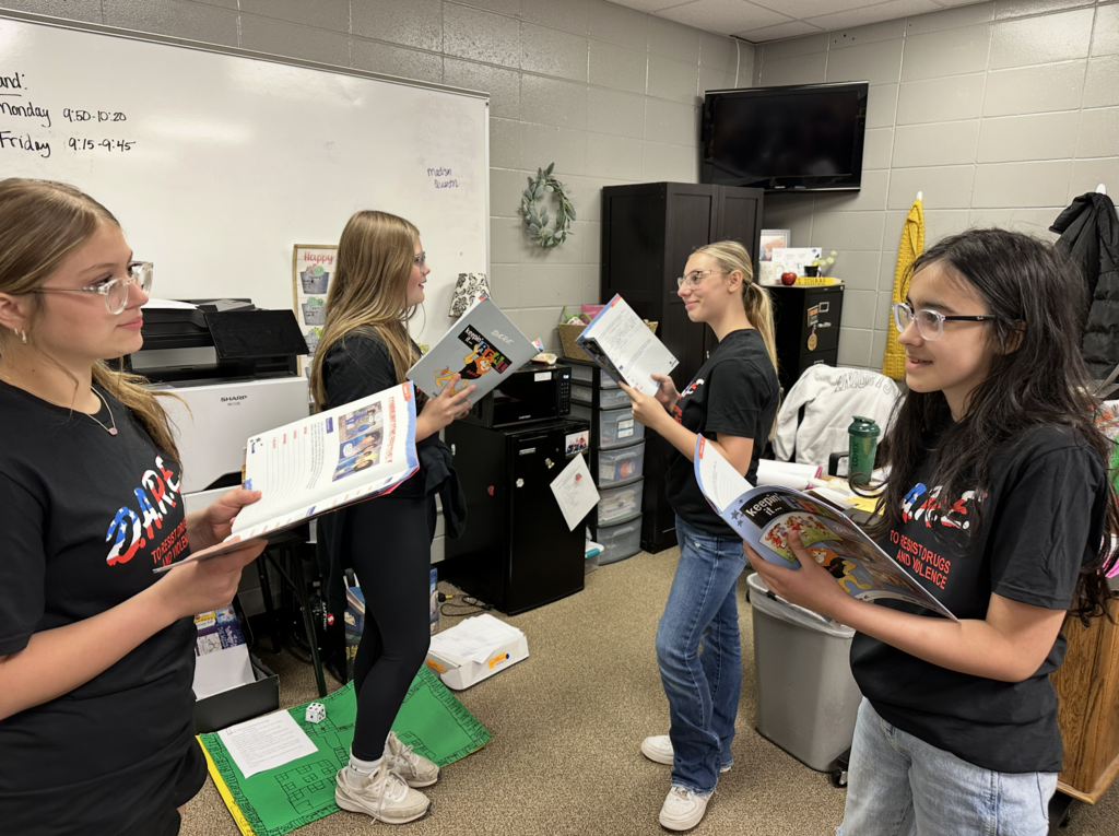 Four girls with open workbooks, working through role playing situations within the D.A.R.E. curriculum.