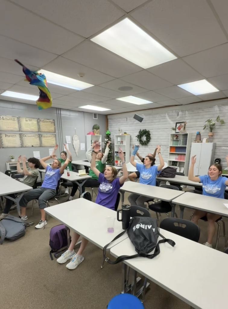 Students sitting at desks in their class with their hands up in the air