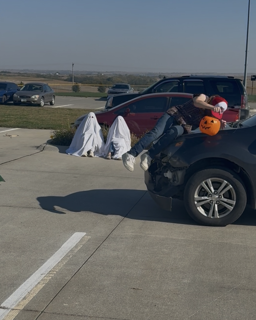 Two students dressed as ghosts and sitting outside on the curb in the parking lot