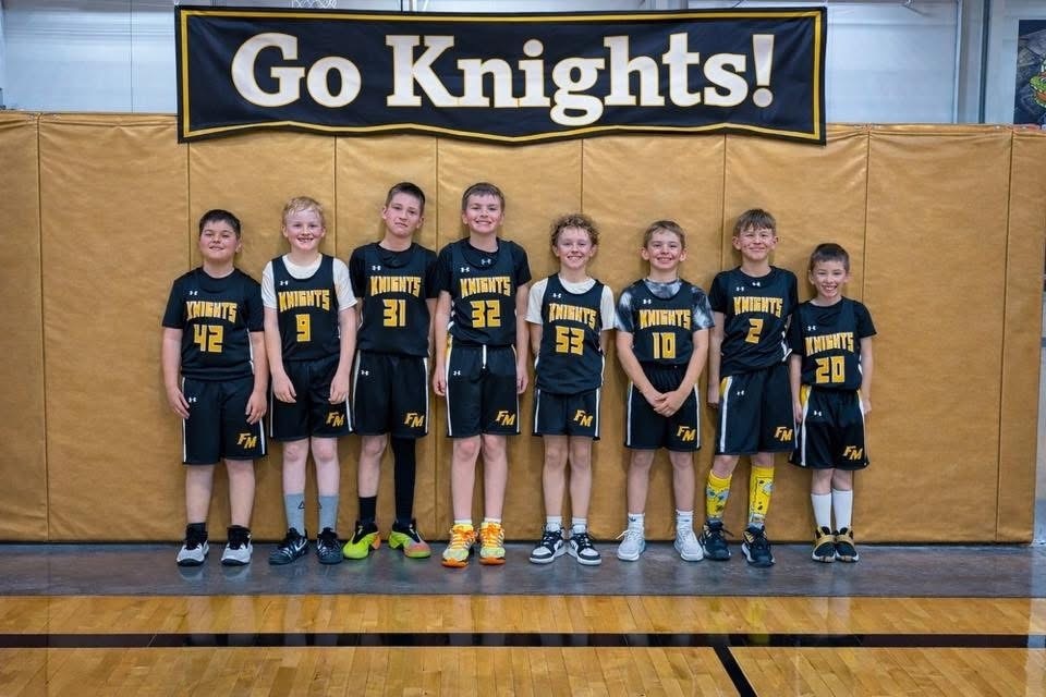 young students wearing Fremont-Mills basketball uniforms in the gym under a banner that says, "Go Knights!"