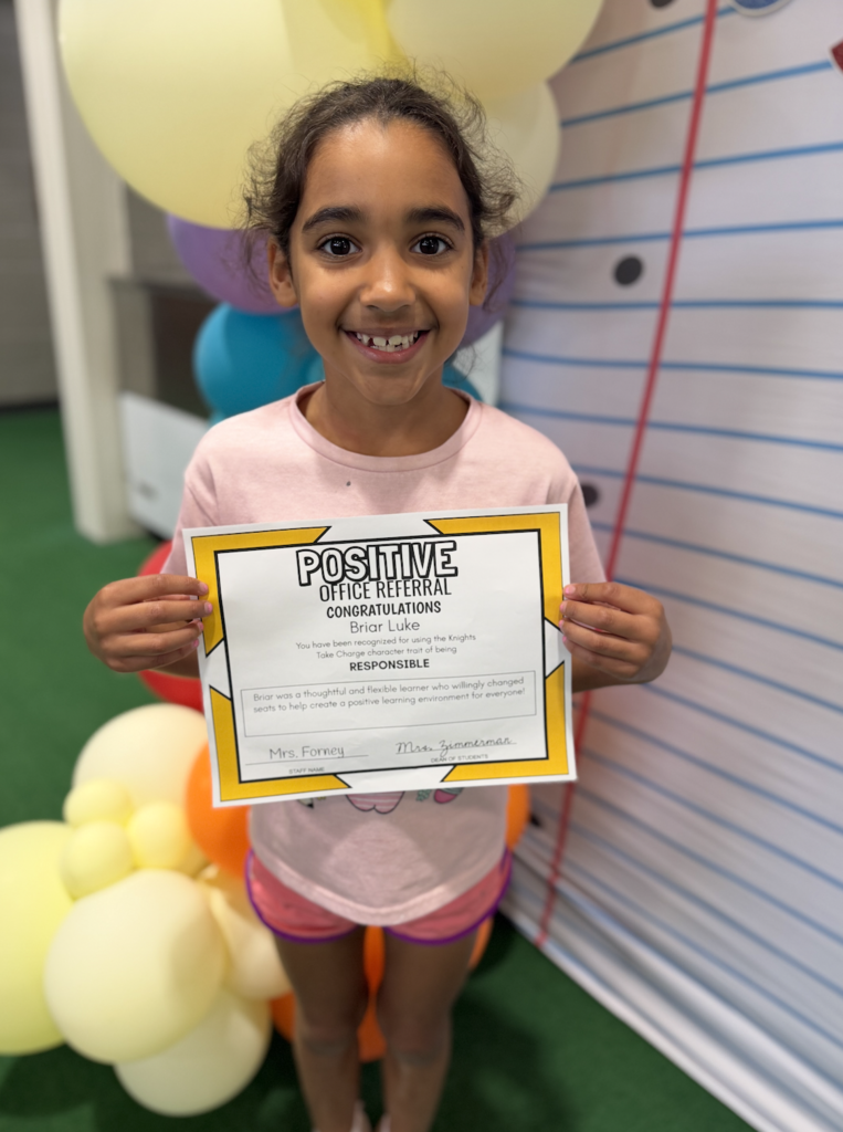 Young girl stands proudly with her Positive Office Referral certificate