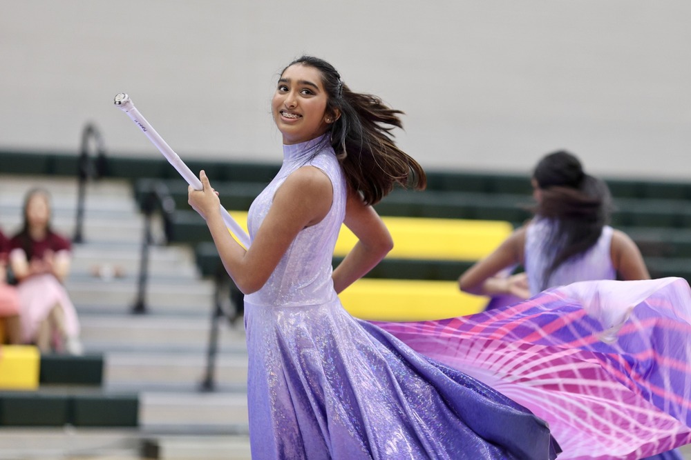 Girl wearing purple holding a winter guard flag and smilihng