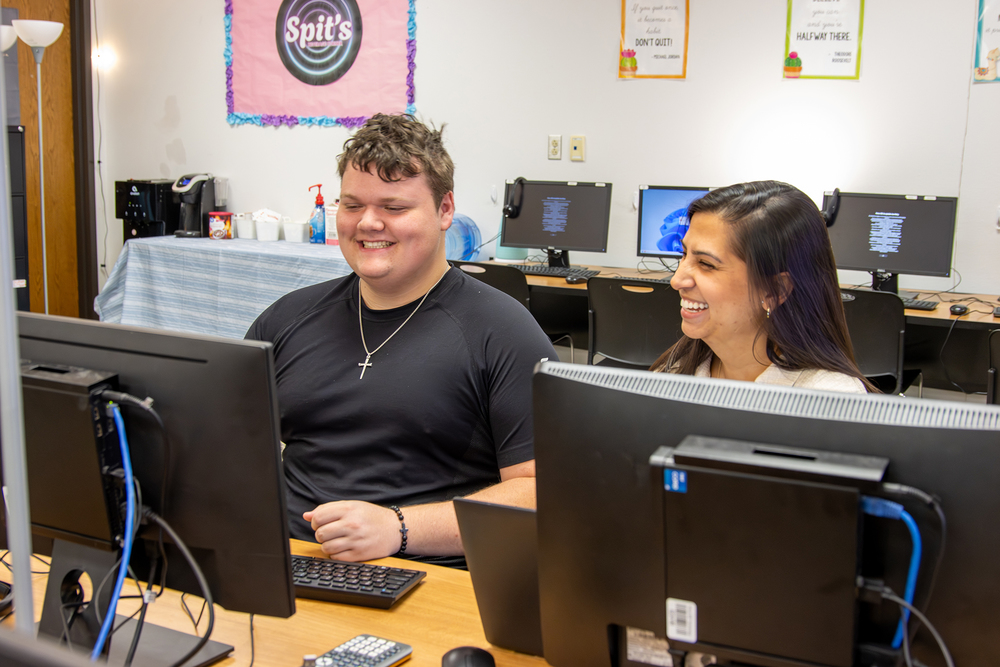 A student and a teacher smiling while looking at a computer