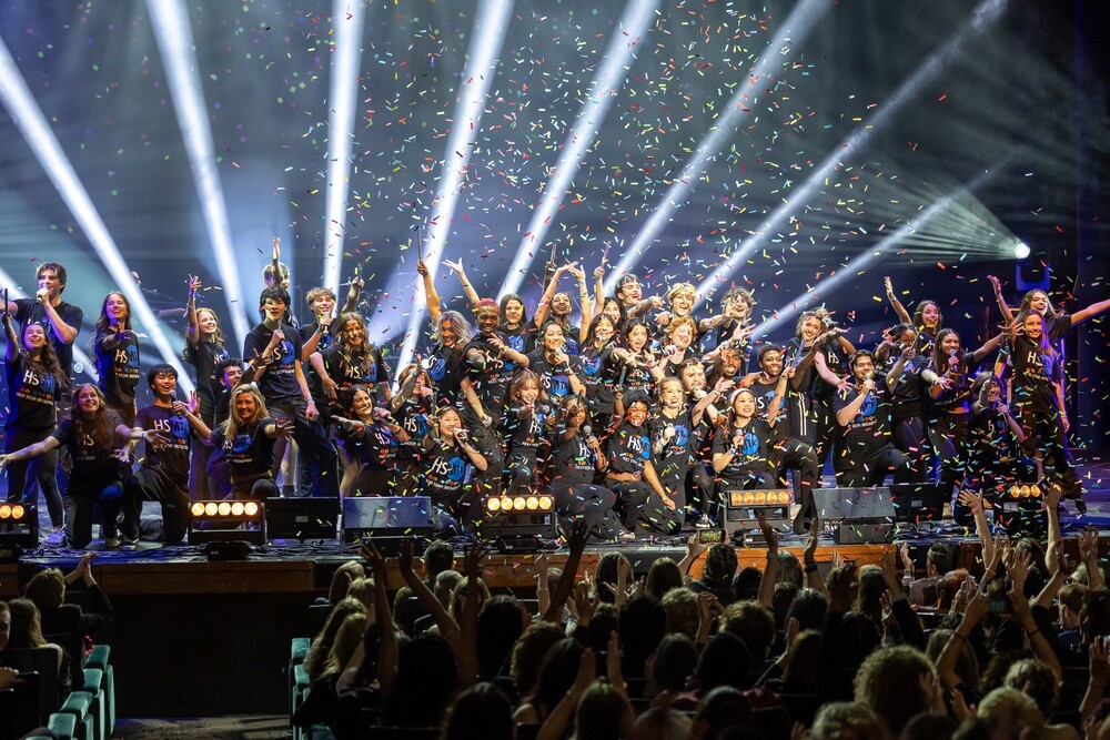 A group of students singing and celebrating on stage with confetti and lights