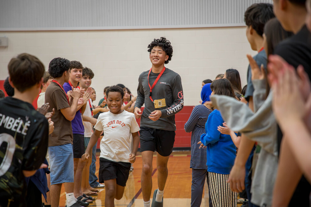 Middle schooler and high schooler running between two lines of cheering students
