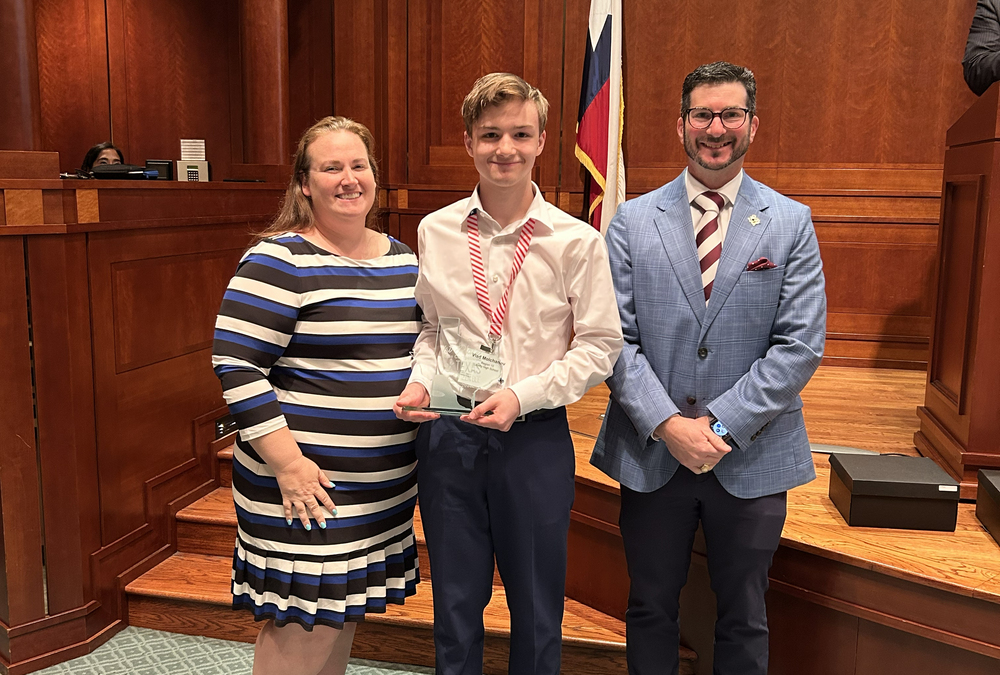 A student holding an award, flanked by two adults
