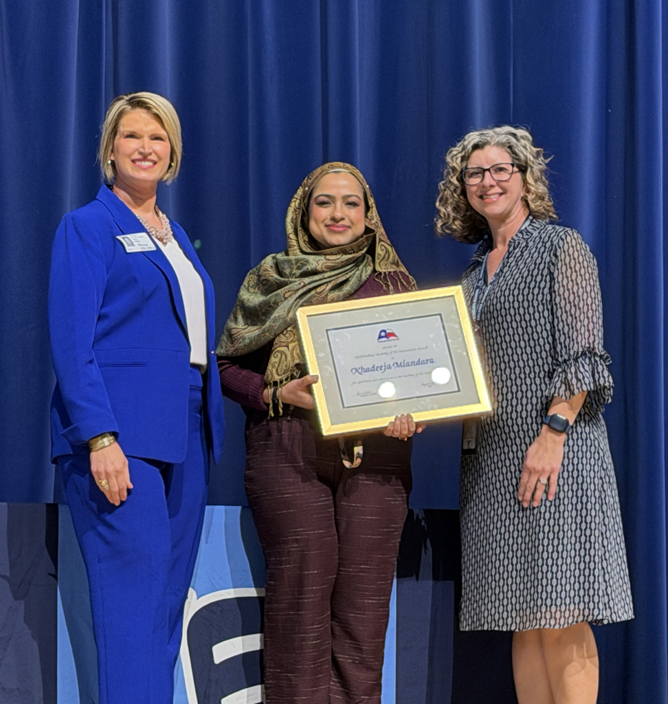 Three people smiling and posing, with the middle person holding a framed certificate