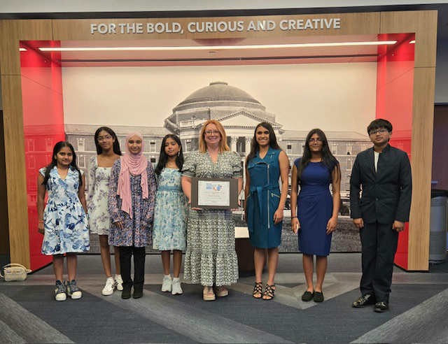 A teacher holding a certificate, next to a group of students