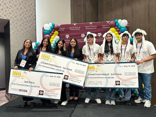 A large number of students holding large checks and posing in front of a photo opp