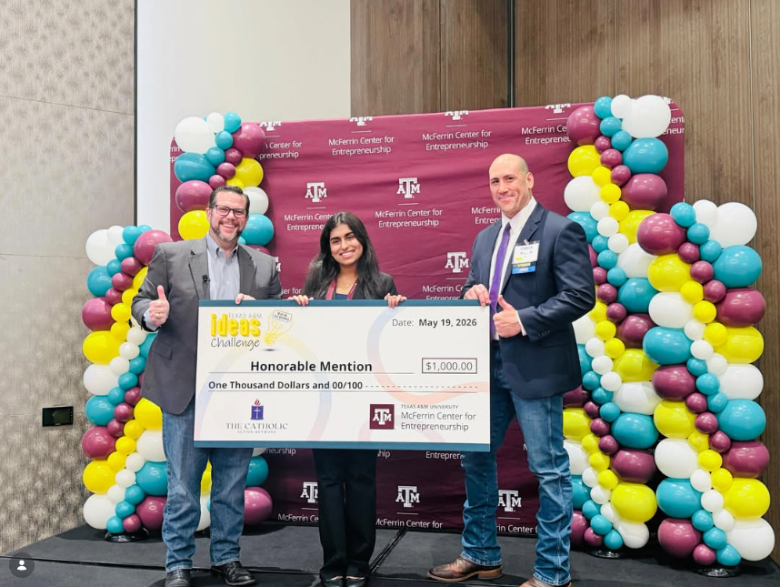 A girl holding a large check that says Honorable Mention, flanked by two adults in front of a photo opp