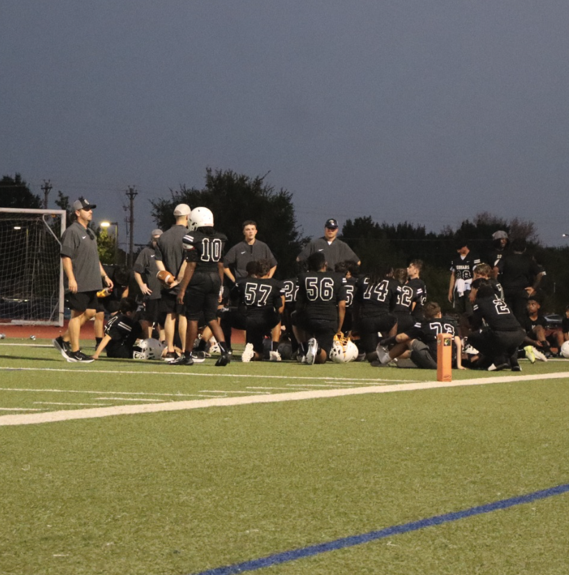 Cougars football players gather around their coaches on the sideline during an evening game.