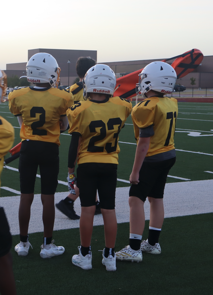 football players watch on as teammates on the field get ready
