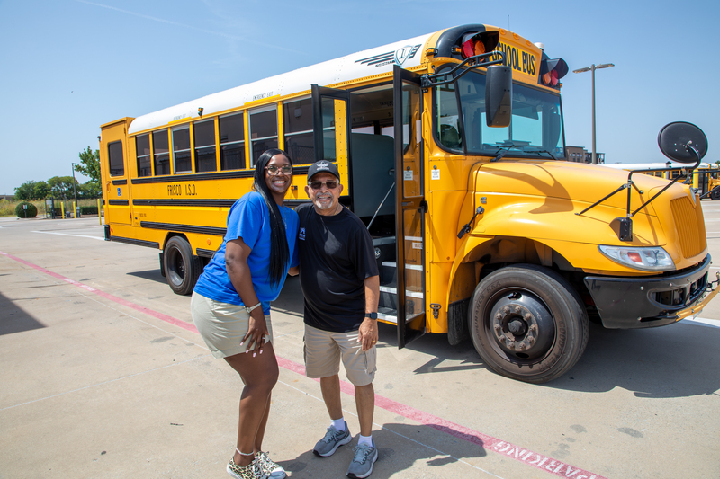 A bus driver and monitor posing in front of a school bus