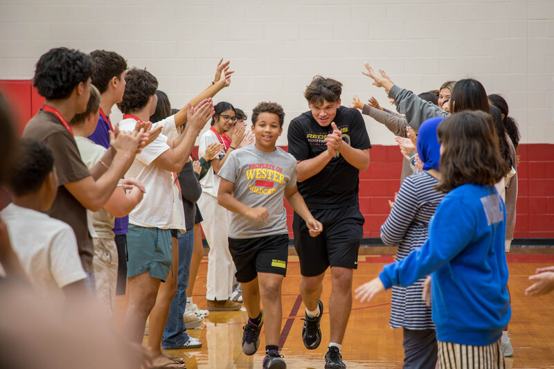 A high schooler and middle schooler run between two rows of students