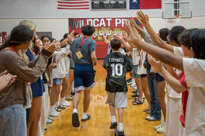 A high schooler and middle schooler run between two rows of students