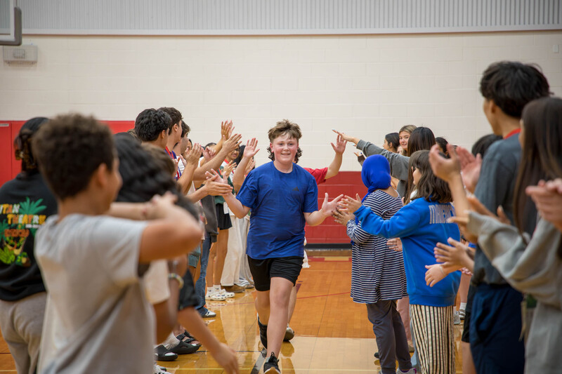 A high schooler and middle schooler run between two rows of students
