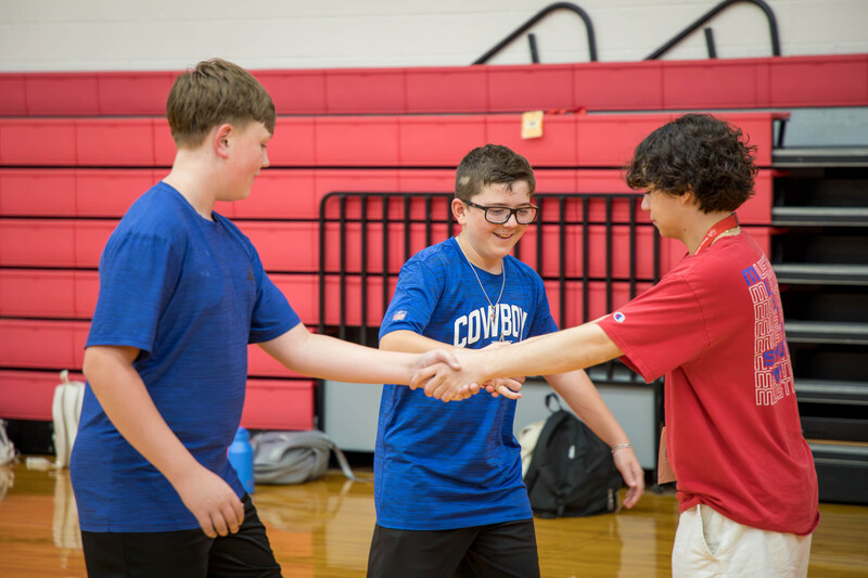 One high schooler and two middle schoolers work on their secret handshake