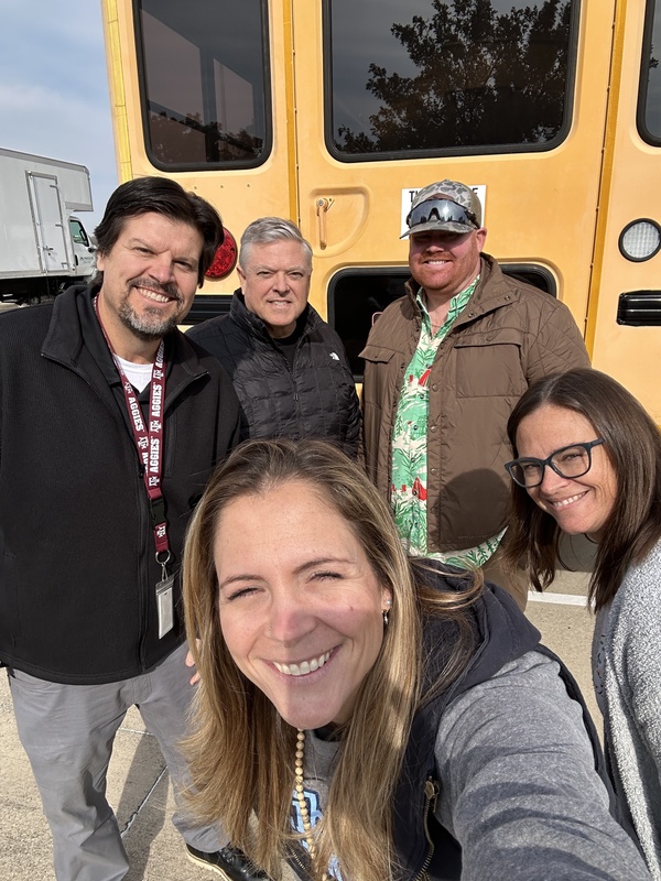 Two women and three men in front of a yellow school bus
