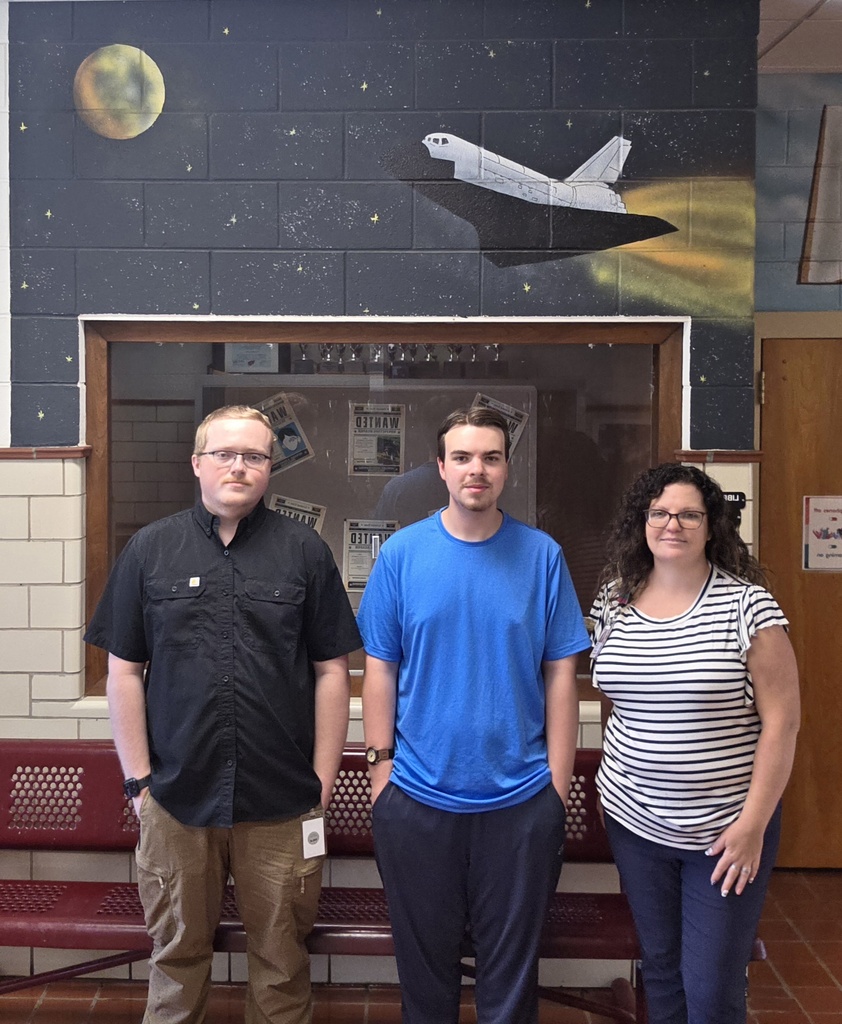 Three people stand in front of a mural with a shuttle, moon, and stars.
