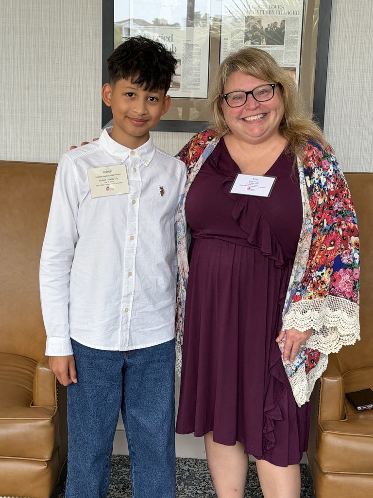 A boy in a white shirt and a woman in a floral-print cardigan stand together, smiling.