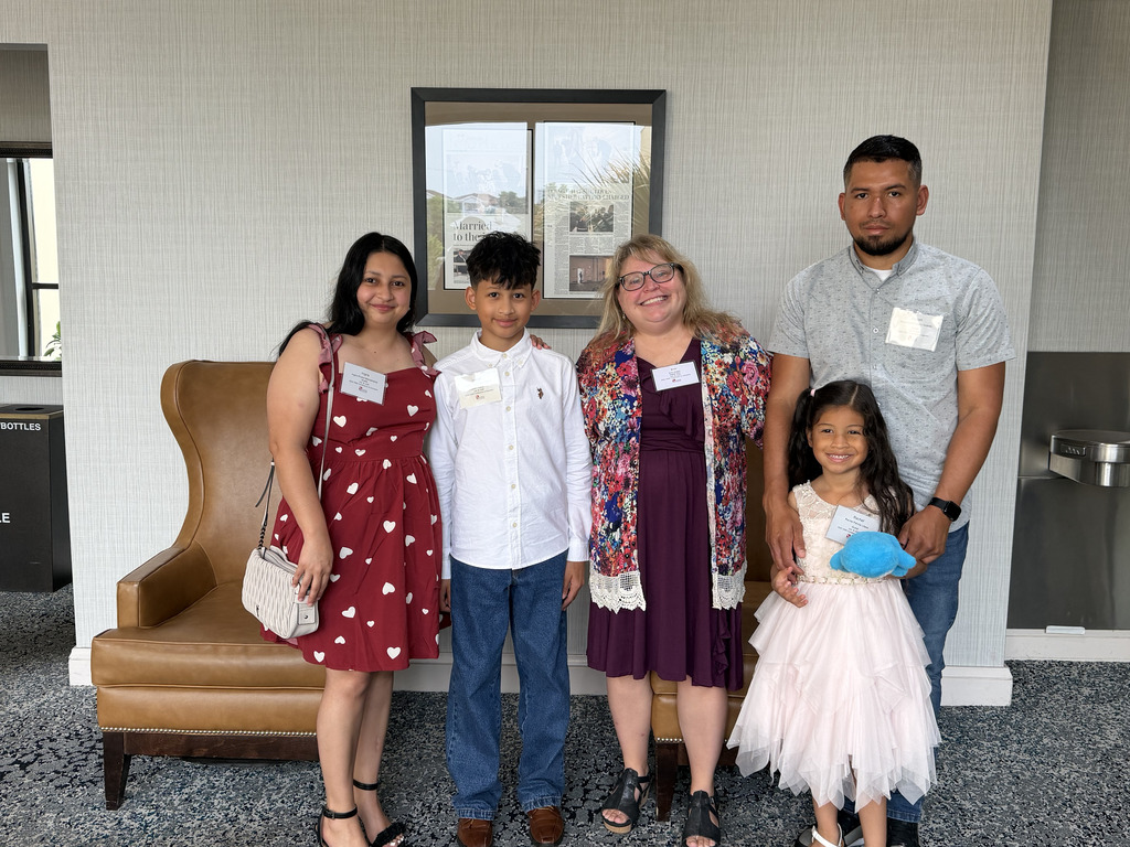 A family of four, two adults and two children, pose together in a room with a large window.