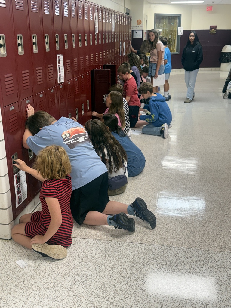Several kids and adults are in a hallway. Some of the children are kneeling while others are standing.
