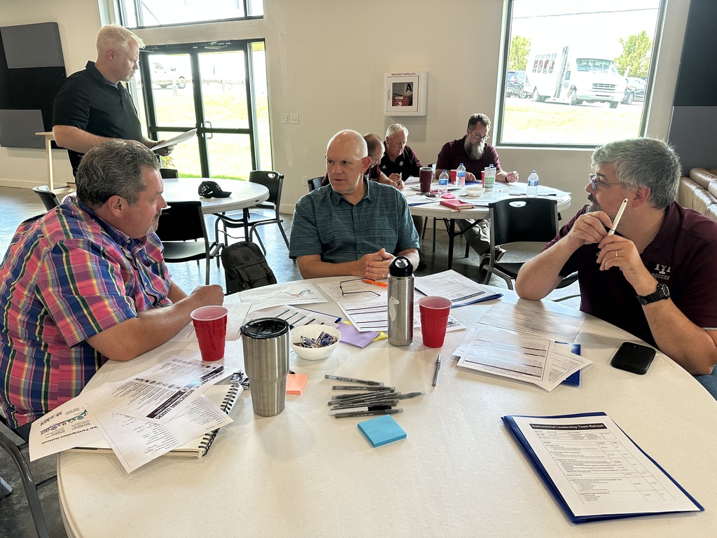 A group of adults sit around a table in a conference room, looking at papers and writing.