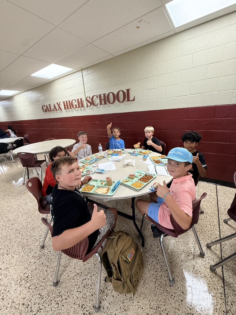 A group of young people sit around a table in a school cafeteria, some wearing hats.