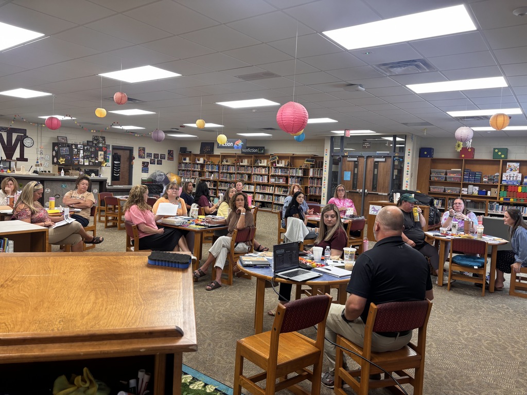 A group of educators in a library sitting at round tables having a discussion