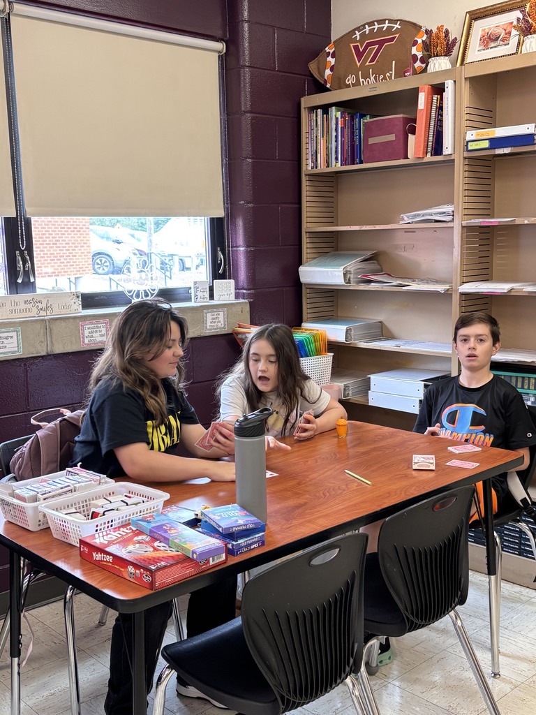 Three people are sitting at a desk. There are books on shelves in the background.