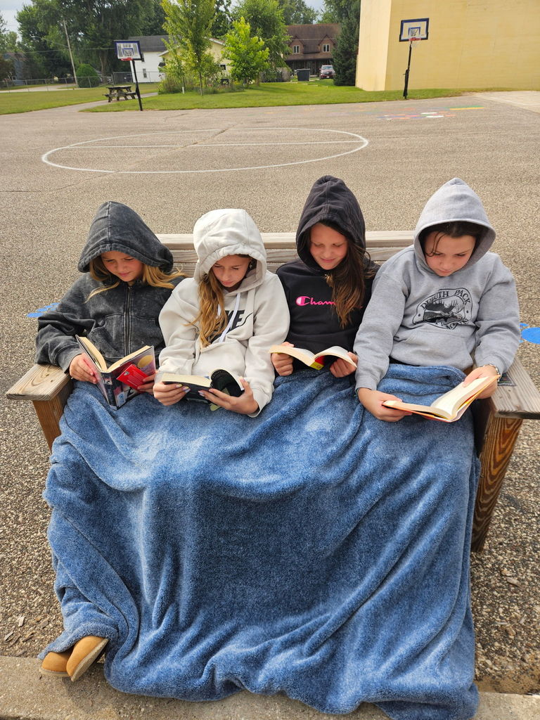 Students reading books on a bench under a blanket