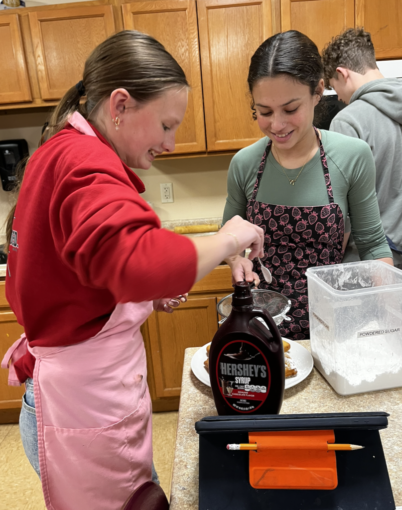 Students sprinkle powdered sugar on their finished Beignets. A French-style, deep-fried pastry made from yeast dough
