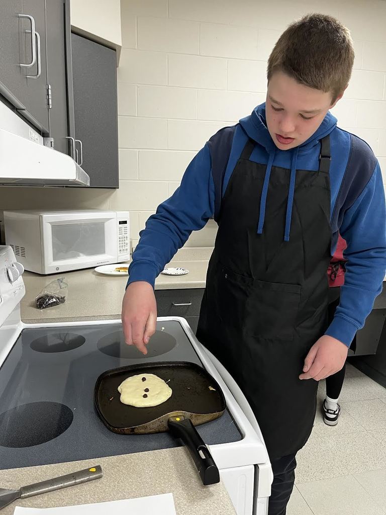 A student adds chocolate chips to their pancake. 