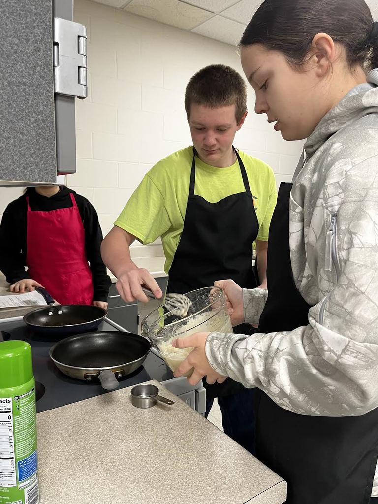 Two students start pouring pancake batter onto the griddle. 