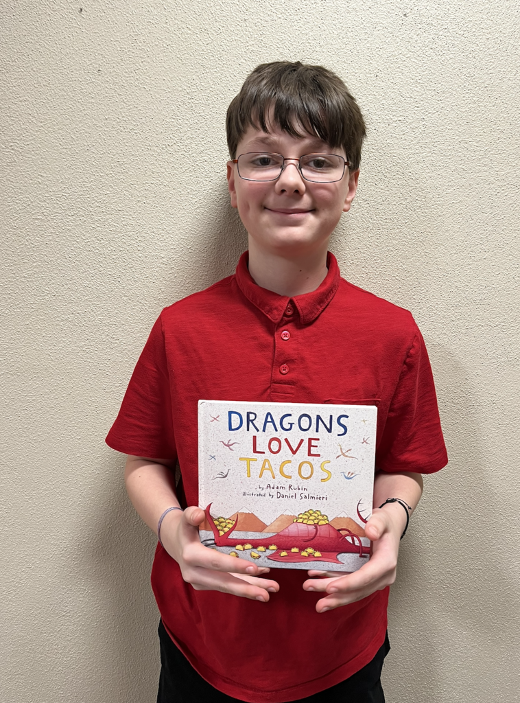A student showing their book "Dragons Love Tacos" for their Children's Literature project. 
