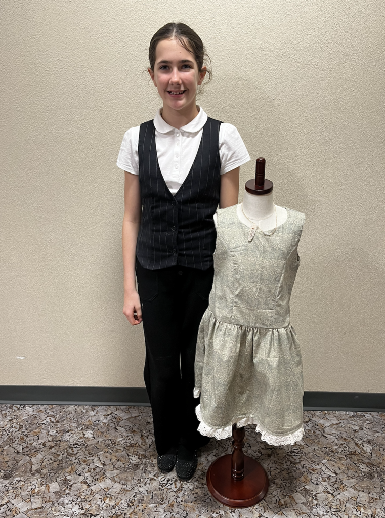 A student standing next to their completed dress for Fashion Construction.