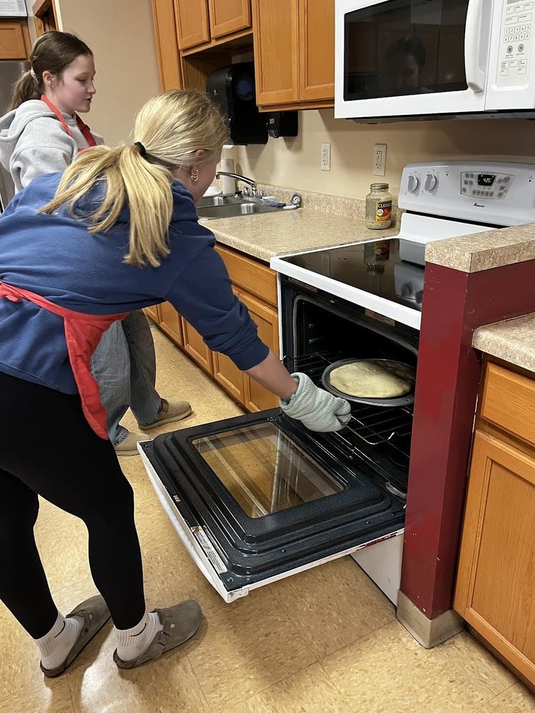 A student places their pizza in the oven.