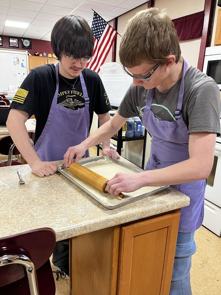Two students work together to roll out their pizza dough.