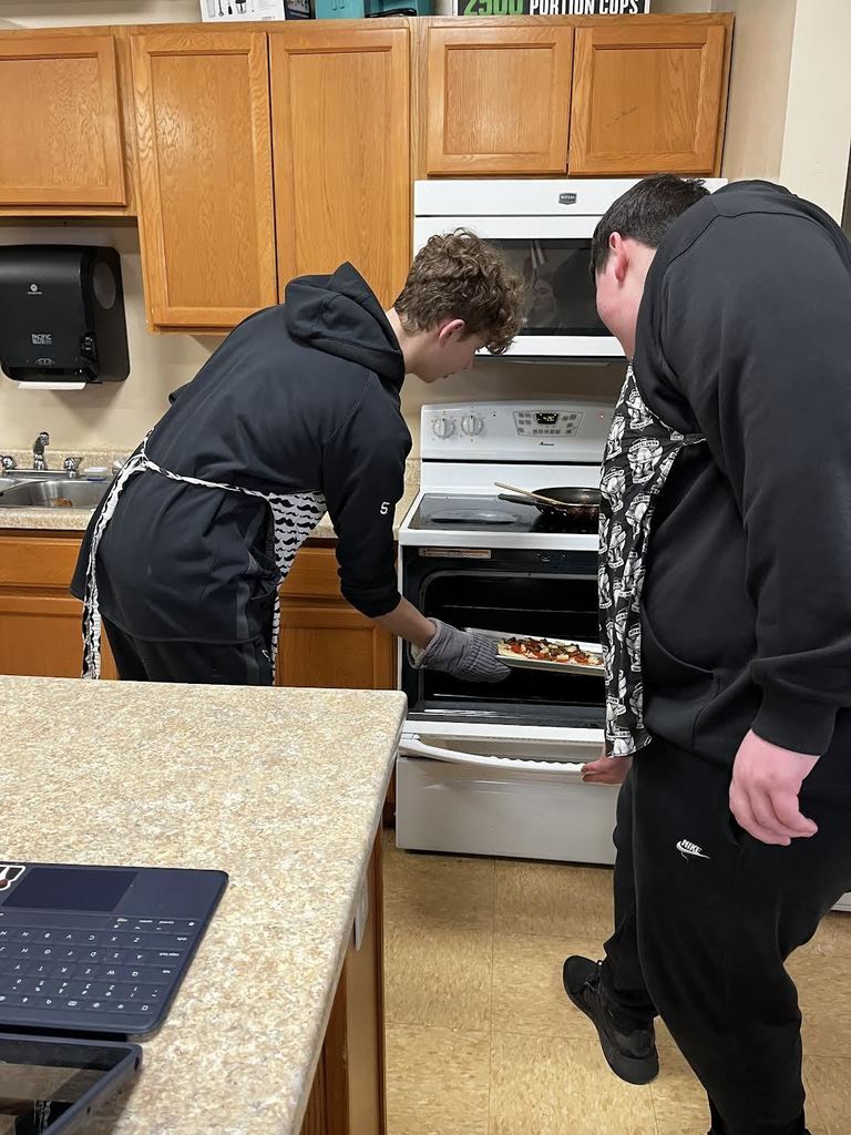 Students work together to place there pizza in the oven.