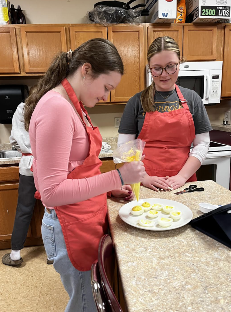 Two students fill their egg whites to complete their deviled eggs.