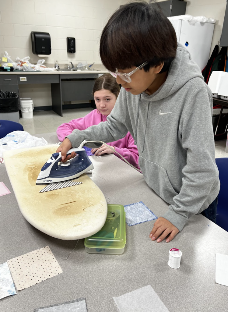 A student irons their bookmark fabric.