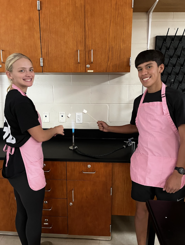 Two students carefully roast their marshmallows over the flame.