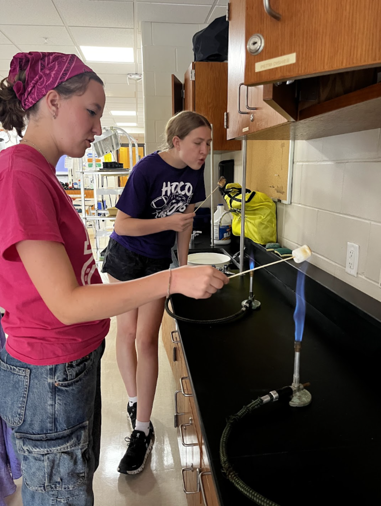 Two students carefully roast their marshmallows over the flame.